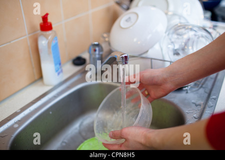 Washing of the dishes - woman hands rinsing dishes under running water in the sink Stock Photo