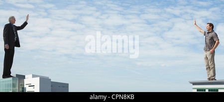 Oversized men standing on rooftops, waving at each other Stock Photo