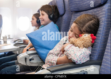 Girl sleeping on airplane holding stuffed animal Stock Photo