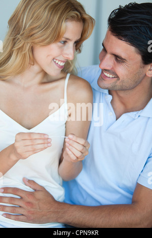 Couple looking at pregnancy test, man with hand on woman's abdomen Stock Photo