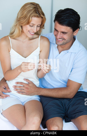 Couple looking at pregnancy test, man with hand on woman's abdomen Stock Photo