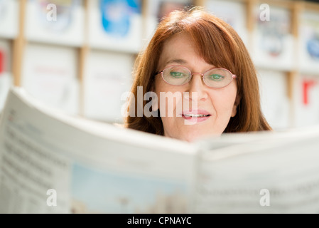 Portrait of middle aged woman with eyeglasses reading paper in library Stock Photo