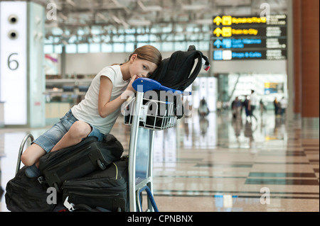 Girl sitting on top of luggage in airport Stock Photo