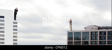 Oversized men standing on rooftops, talking to each other through tin can phones Stock Photo