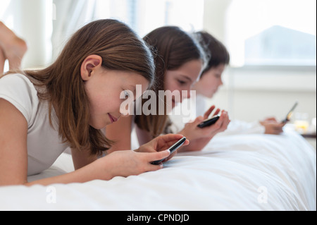 Siblings lying on bed playing handheld video games Stock Photo
