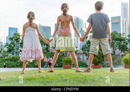 Young siblings standing on grass holding hands, rear view Stock Photo
