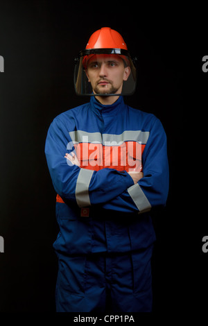 The worker in overalls and a helmet on a black background Stock Photo
