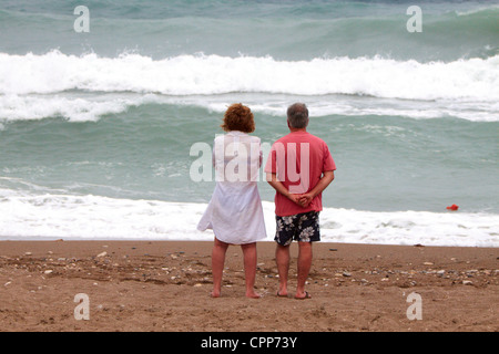 Old couple watch large waves on Afandou beach while on holiday in Rhodes Greece Stock Photo