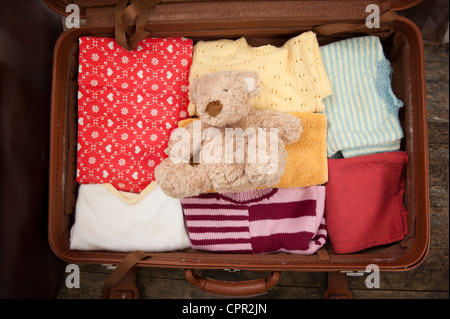 Open suitcase with clothes and teddy bear Stock Photo