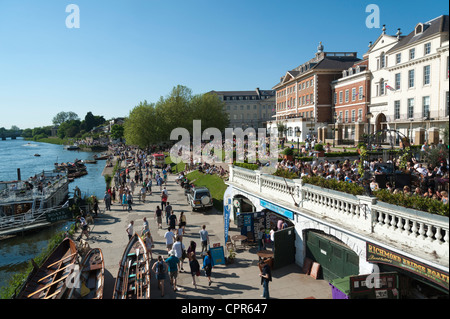 The Riverside walk along the River Thames Richmond London on a sunny day with crowds of people sitting on the grass in summer. Stock Photo