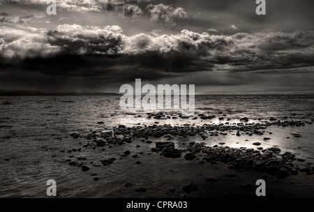 Dark storm clouds gathering over a rocky beach near Homer, Alaska overlooking the Kachemak Bay in black and white. Stock Photo