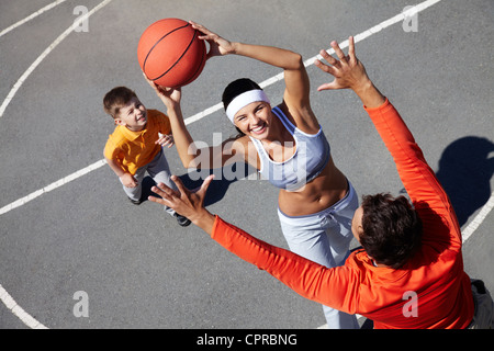 Image of happy female going to throw ball into basket with man and