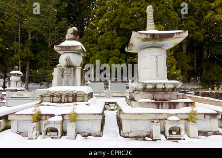 Koya Okunoin cemetery in the snow with two large stone memorials one in the shape of a five stone tower and the other in a stone pagoda. Japan. Stock Photo