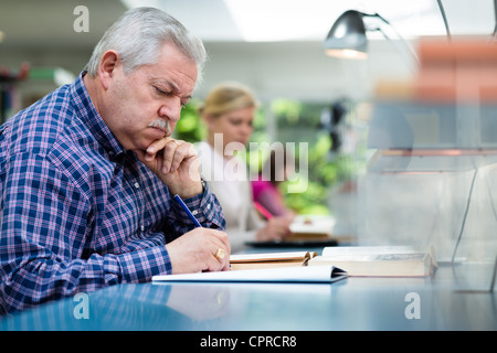 Elderly man studying with a group of young college students in library and taking notes Stock Photo