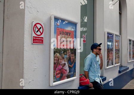 Man smoking next to a no smoking sign Stock Photo