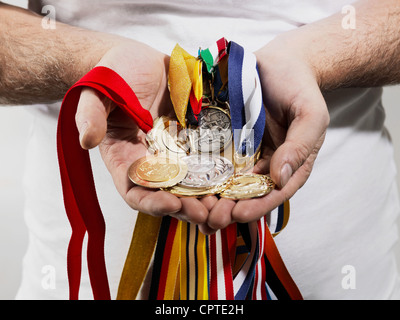 Mature man holding gold medals against white background Stock Photo