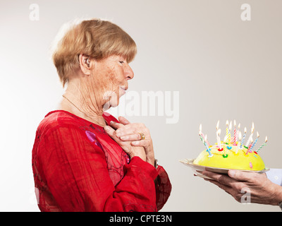 Senior woman receiving birthday cake against white background Stock Photo