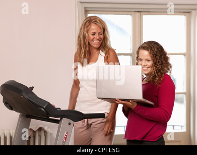 Young woman showing laptop to mother on treadmill Stock Photo