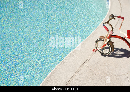 Child's tricycle at edge of swimming pool Stock Photo