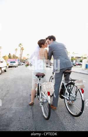 Young newlywed couple kissing on bicycles in street Stock Photo