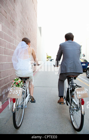 Young newlywed couple cycling along street, rear view Stock Photo