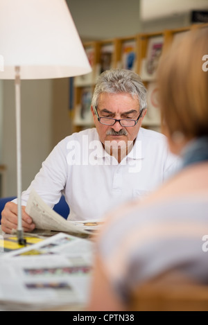 Retired senior people, old man reading news and magazines with wife in library Stock Photo