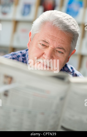 Senior man with mustache reading newspaper in library Stock Photo