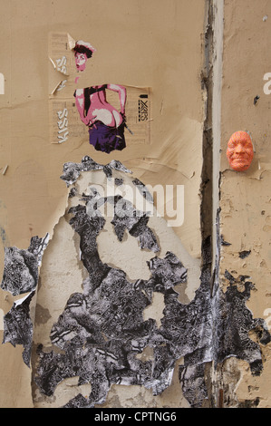 A detail of torn, pealing posters and a brightly painted mask stuck on a roughly textured wall discovered in a Parisian back alley. Paris, France. Stock Photo