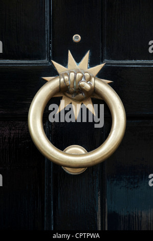 Brass hand star fist door knocker on a black wooden house door. Stow on the wold, Gloucestershire, England Stock Photo