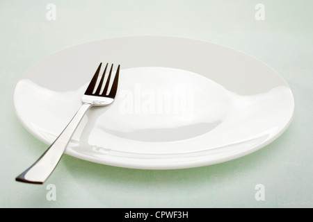 White plate and modern fork on simple plain green background. Stock Photo