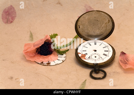 Old pocket watch and poppy on handmade paper with leaves Stock Photo