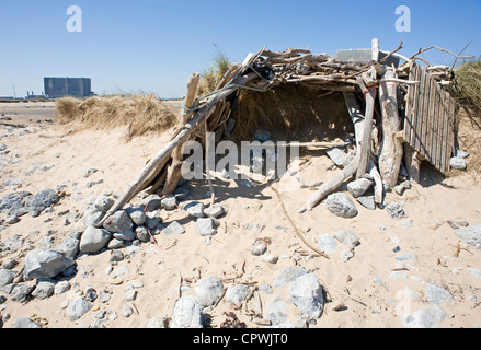 Shelter made from driftwood on North Gare, Teesmouth.  Hartlepool Nuclear power station can be seen in the distance at left. Stock Photo