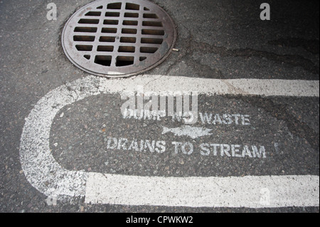 A signs painted on the pavement  warns people not to dump any waste into the drain will drain into the nearby stream. Stock Photo