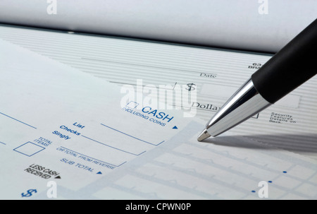 Close up of pen filling out a personal banking deposit slip with check in background and copy space. Stock Photo