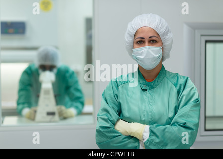 Portrait of woman working in biotechnology research center with man looking through microscope in background Stock Photo