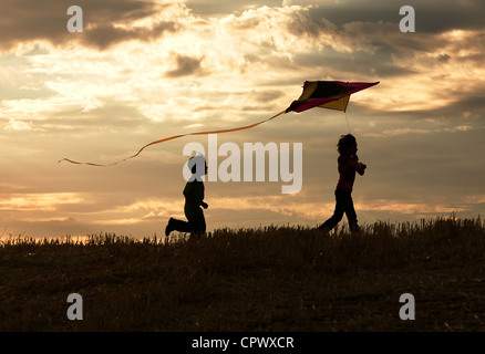 Two children enjoy flying a kite during sunset. Stock Photo