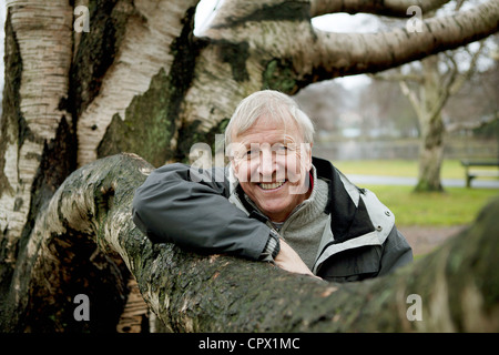 Senior man leaning against tree, smiling Stock Photo