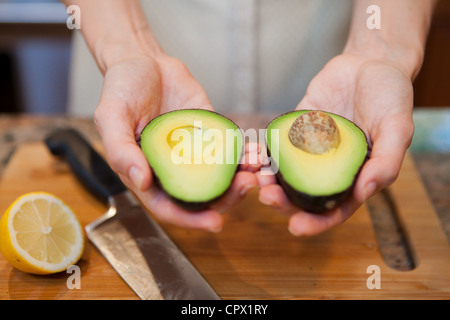 Mid adult woman holding sliced avocado Stock Photo
