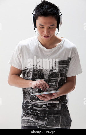 Young Asian man using digital tablet with headphones, studio shot Stock Photo