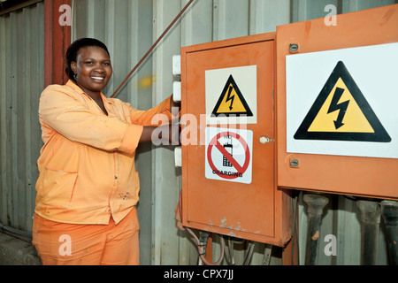 Female black factory worker stands next to an electrical box smiling at camera Stock Photo