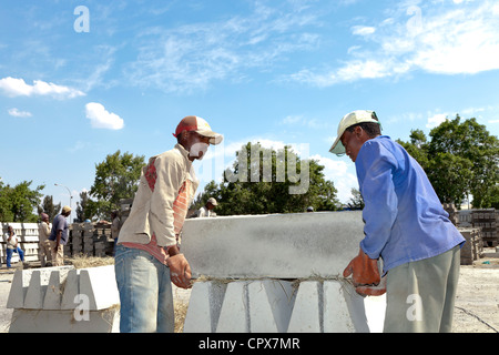Two African construction workers carry a cement block Stock Photo