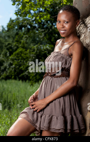 Young adult funky black female leaning against tree smiling at camera Stock Photo