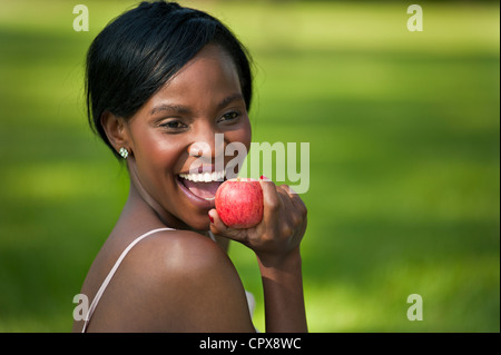 Young African female eating an apple in a park Stock Photo