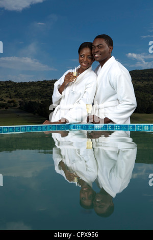 An African couple wearing robes and holding champagne glasses alongside a pool Stock Photo