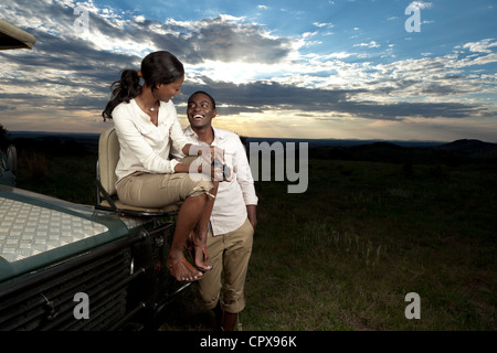 An African couple chatting next to a game viewing vehicle during sunset Stock Photo