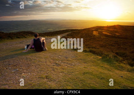 A fell runner resting on top of Moal Famau the highest point in the Clwydian Range Hills as the sun sets over the range and heather Stock Photo