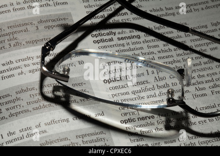 Reading glasses resting on book focusing on word optician Stock Photo