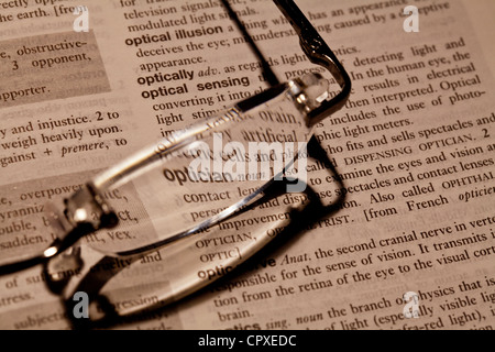 Reading glasses resting on book focusing on word optician Stock Photo
