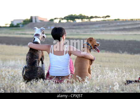 Young woman sitting in nature with her dogs, at sunset Stock Photo