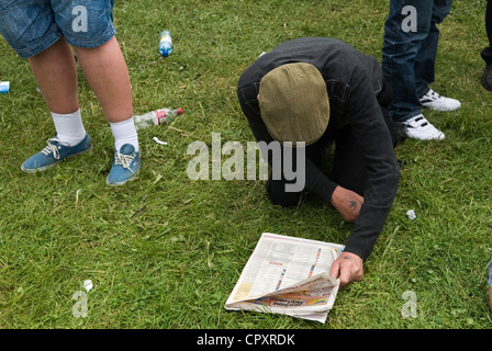 Man wearing flat cap on the ground reading the sporting pages of a newspaper, he is checking the runners and their odds. He has Swallow tattoo on his hand  he is a former sailor.  Derby Day, Epsom Downs Surrey UK 2012  2010s  HOMER SYKES Stock Photo